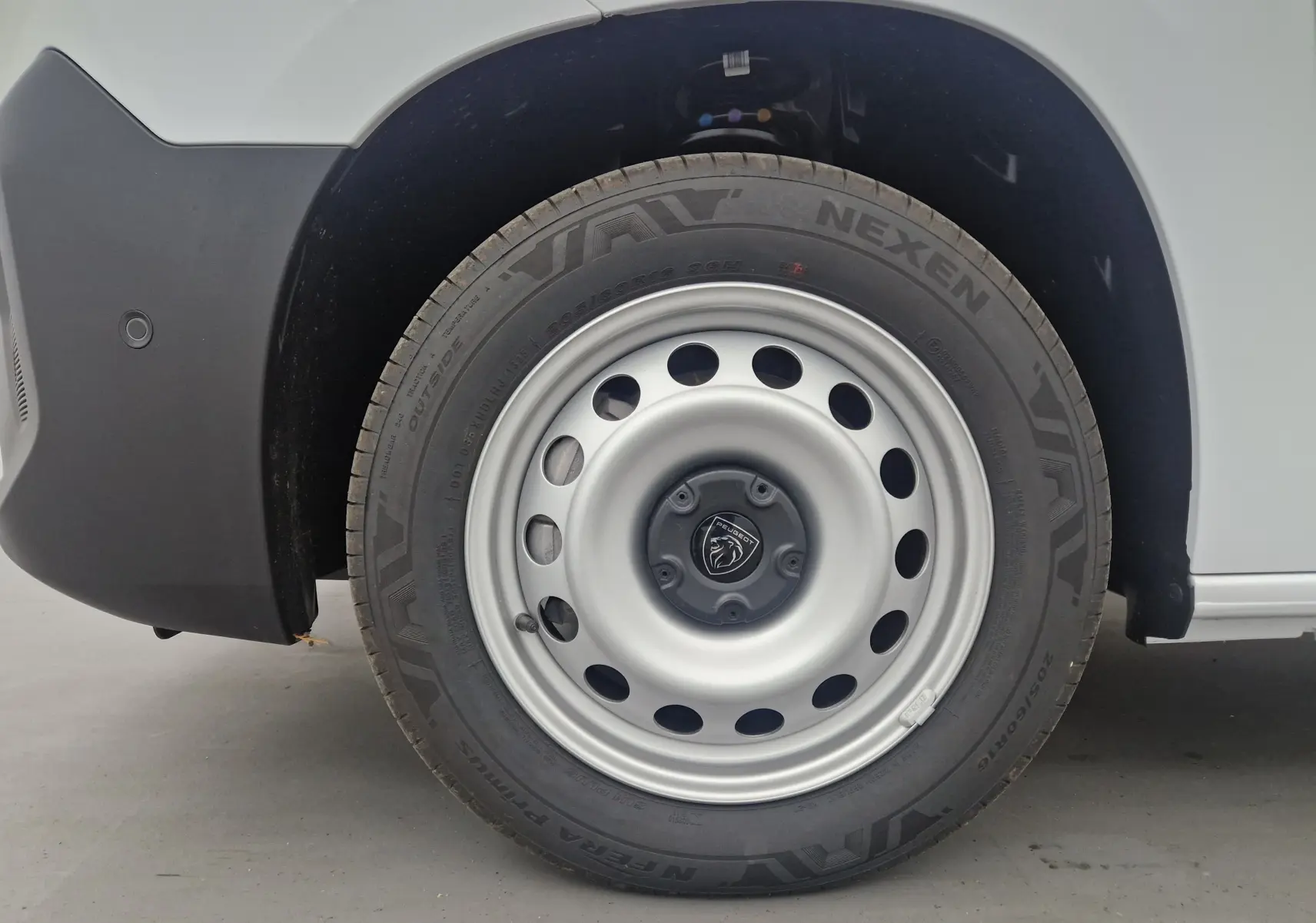 Gros plan sur la roue avant gauche blanche du Peugeot Partner 2025 avec jante acier et logo Peugeot au centre.