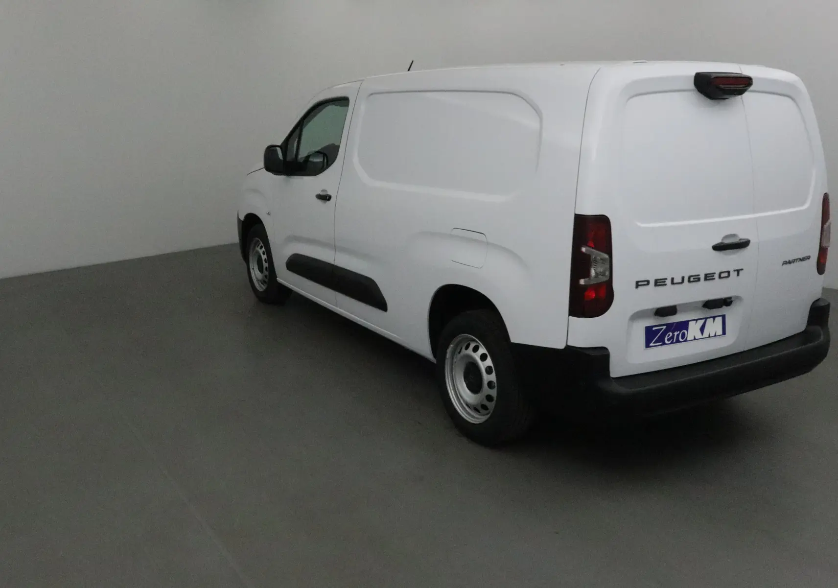 Vue 3/4 arrière droite d'un Peugeot Partner blanc utilitaire avec logo et plaque ZeroKM visible.