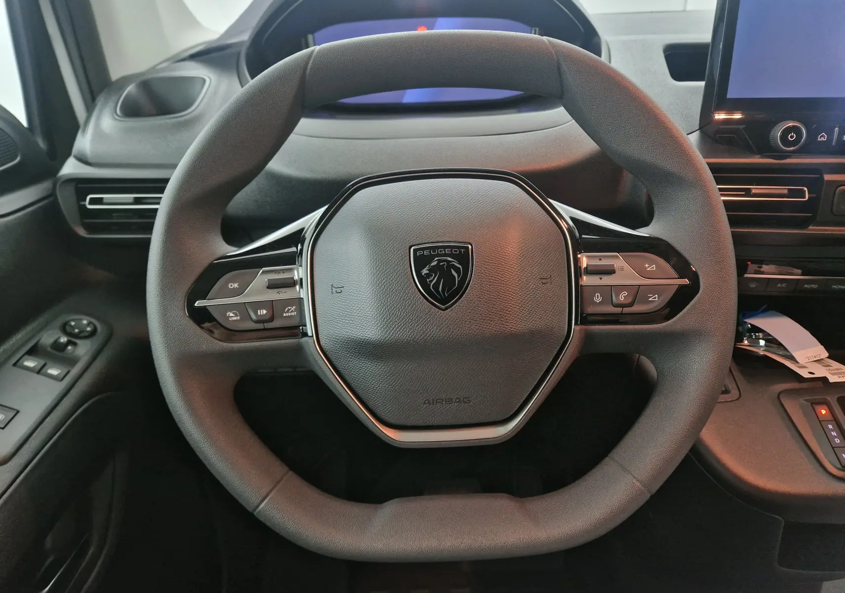 Gros plan sur le volant multifonction noir du Peugeot Partner 2025, avec logo lion au centre et commandes intégrées.