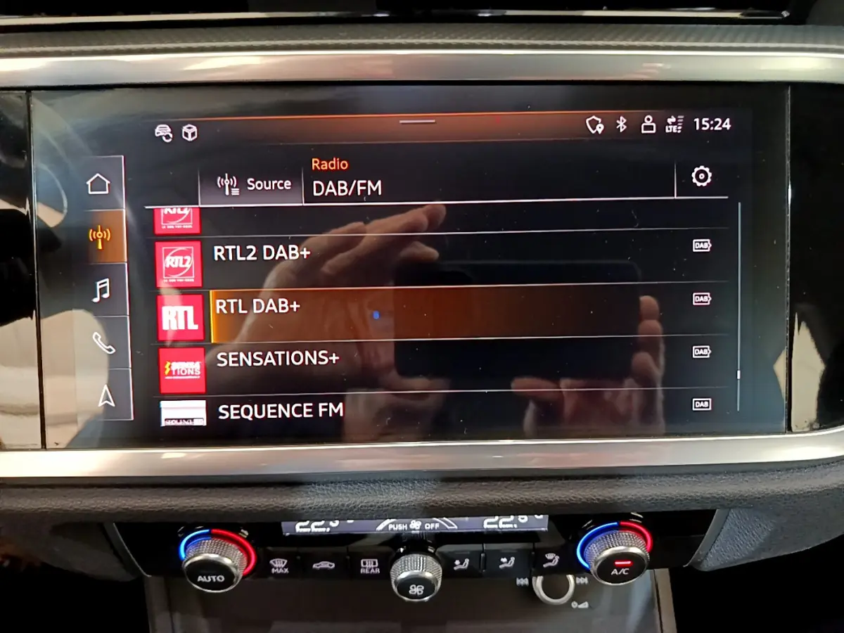 Écran tactile central affichant les stations radio DAB/FM dans l'habitacle d'un Audi Q3 noir, vue de face rapprochée.