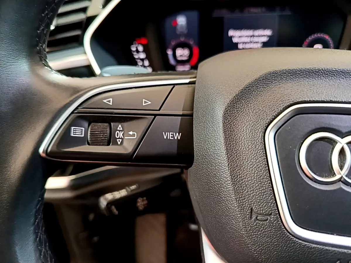 Gros plan sur le volant cuir noir d’un Audi Q3 35 TDI 2021, avec commandes multifonctions et logo Audi central.