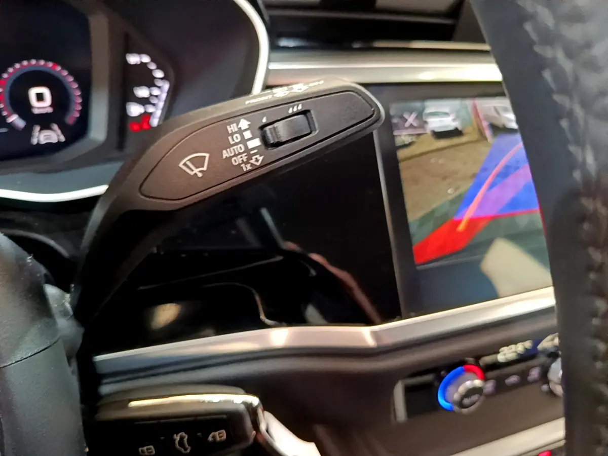 Gros plan intérieur sur le commodo d’essuie-glace et l’écran tactile avec caméra de recul de l’Audi Q3 noir, vue côté conducteur.