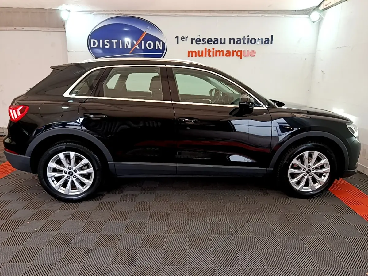 Vue de profil côté gauche d’un Audi Q3 noir 2021 avec jantes alliage et rails de toit chromés en intérieur showroom.