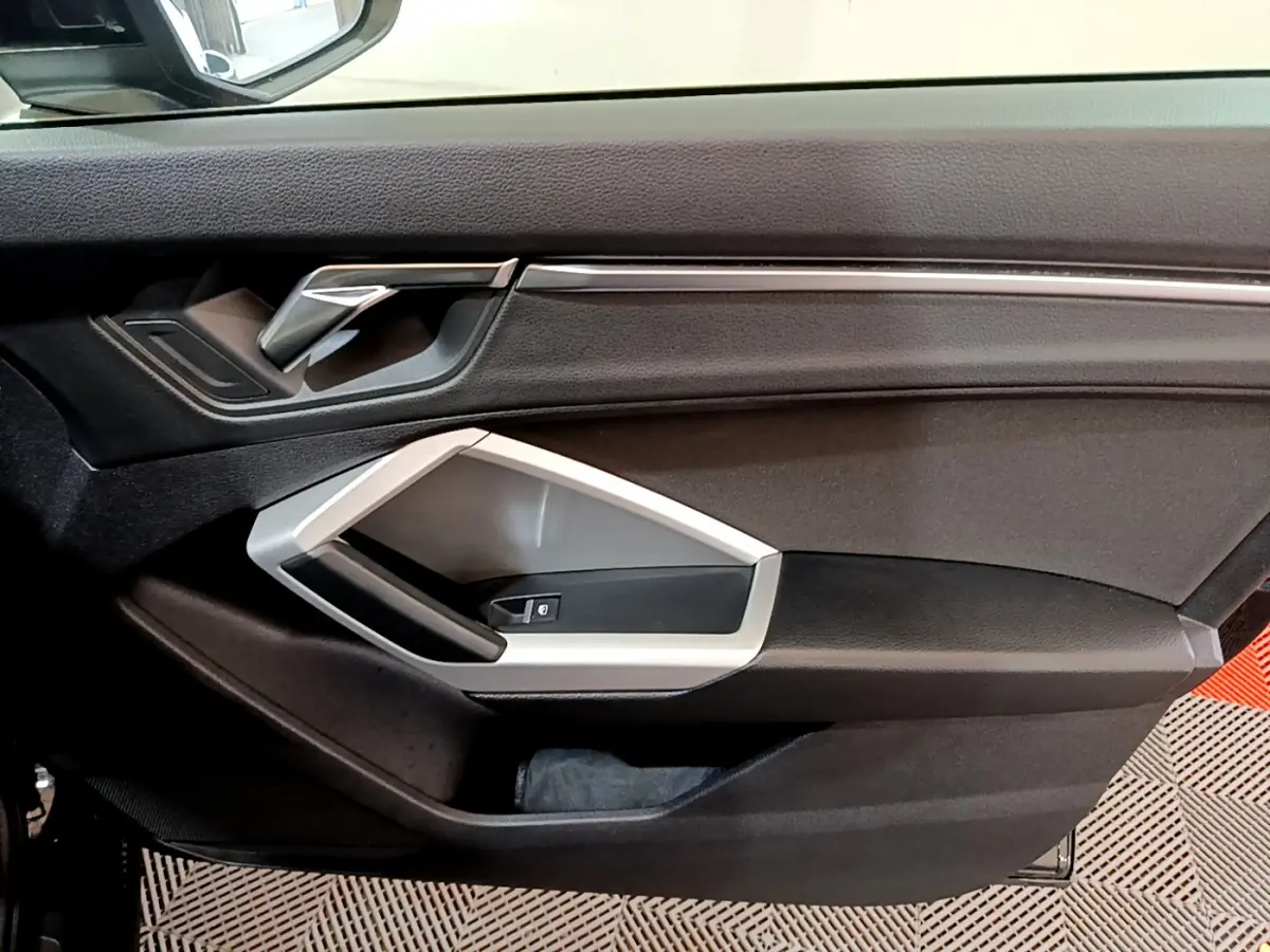 Vue intérieure du panneau de porte avant gauche noir avec poignée argentée et commande de lève-vitre Audi Q3 2021.