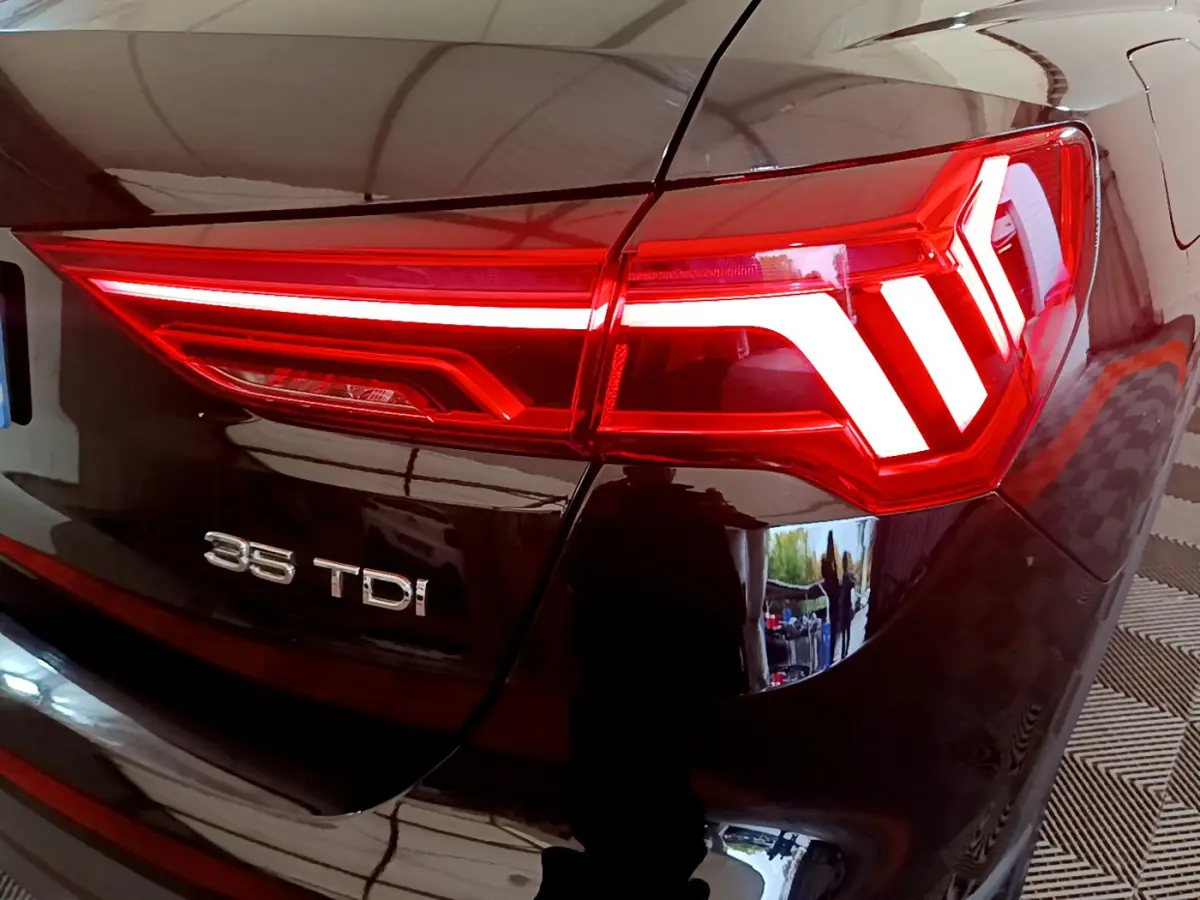 Gros plan sur le feu arrière droit rouge allumé d’un Audi Q3 noir 35 TDI avec logo visible sur le coffre.