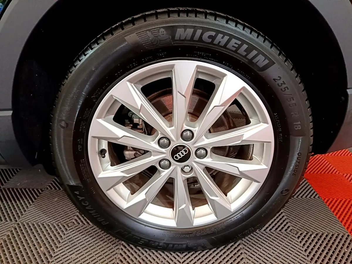 Gros plan sur la jante alliage argentée avec logo Audi au centre, pneu Michelin monté sur Audi Q3 noir.