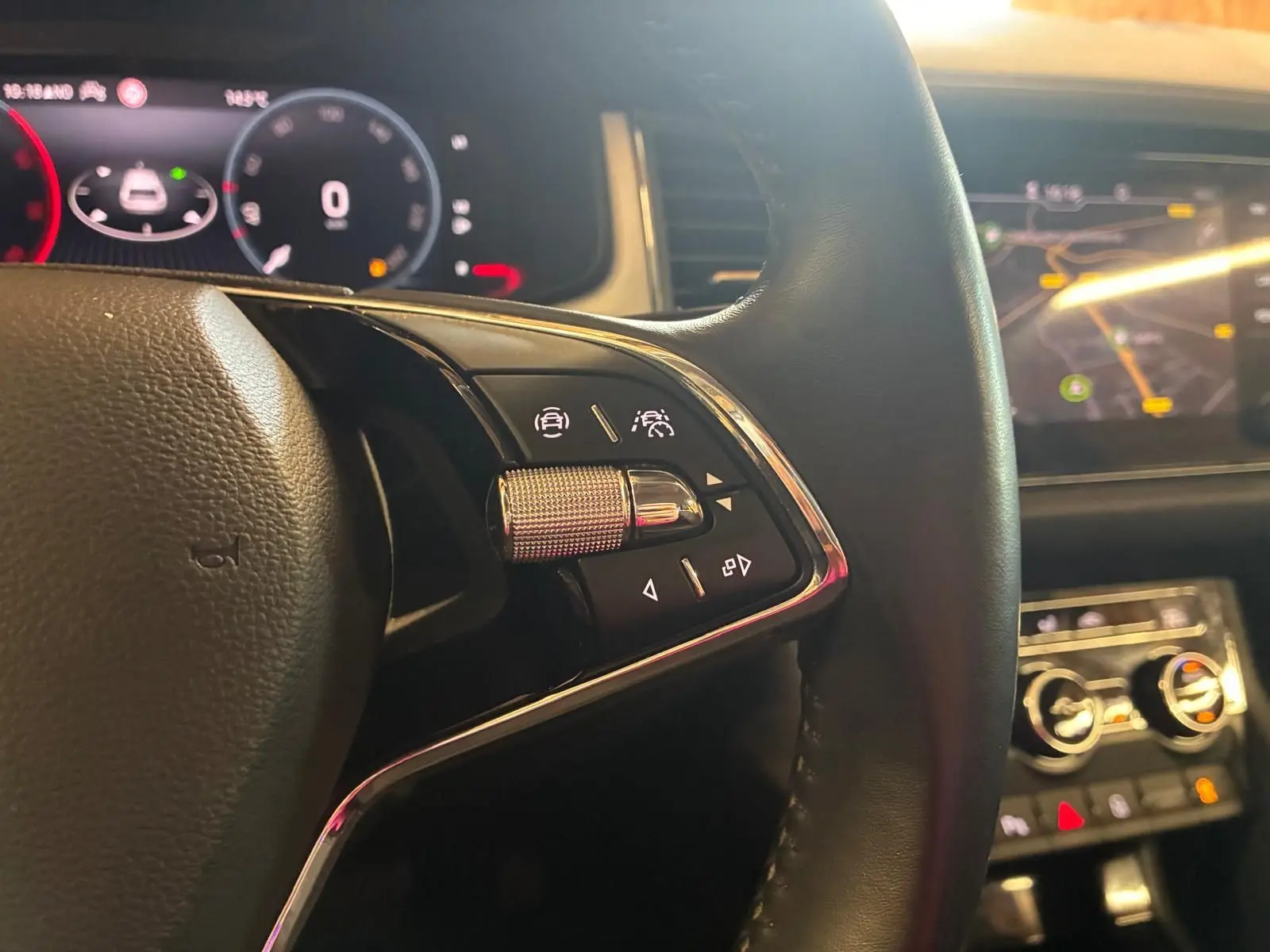 Gros plan sur le volant noir avec commandes intégrées du Skoda Kodiaq 2.0 TDI gris, tableau de bord digital en arrière-plan.