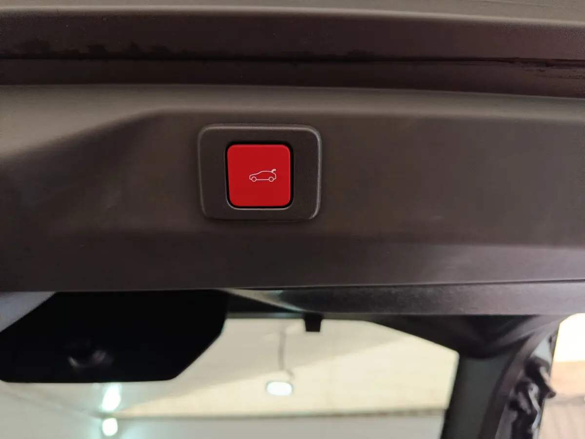 Bouton rouge d'ouverture électrique du coffre sur le hayon intérieur d'un Peugeot 3008 gris foncé hybride 2025