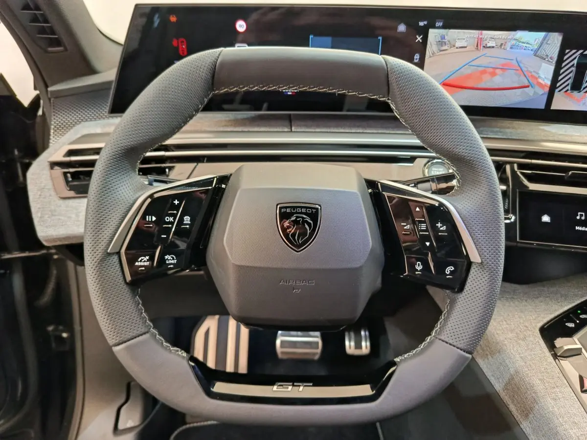 Volant cuir gris du Peugeot 3008 GT 2025 avec commandes multifonctions et écran tactile de recul en arrière-plan.