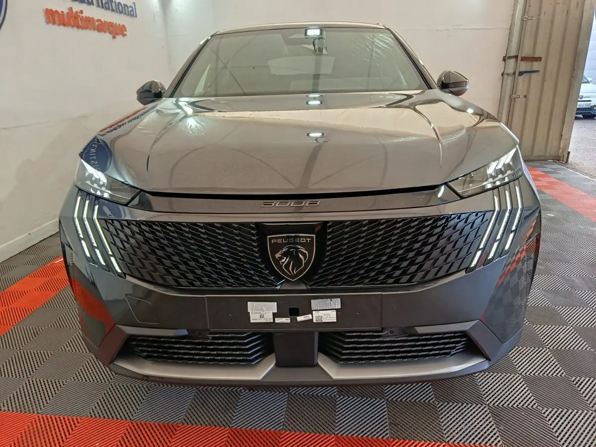 Vue frontale du Peugeot 3008 gris foncé 2025 avec calandre noire et feux LED à griffes distinctifs allumés.