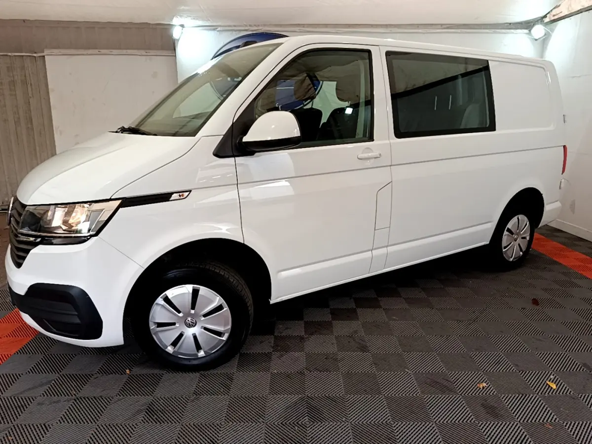 Vue 3/4 avant droit d’un Volkswagen Transporter blanc 2021 avec jantes acier et vitres teintées arrière.