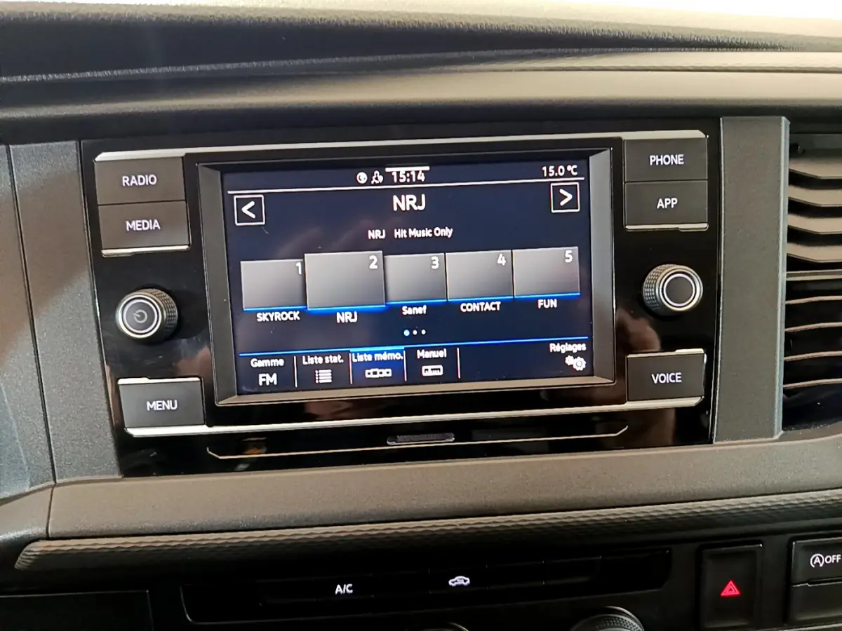 Écran tactile central du tableau de bord du Volkswagen Transporter blanc, affichant la radio NRJ en mode FM.
