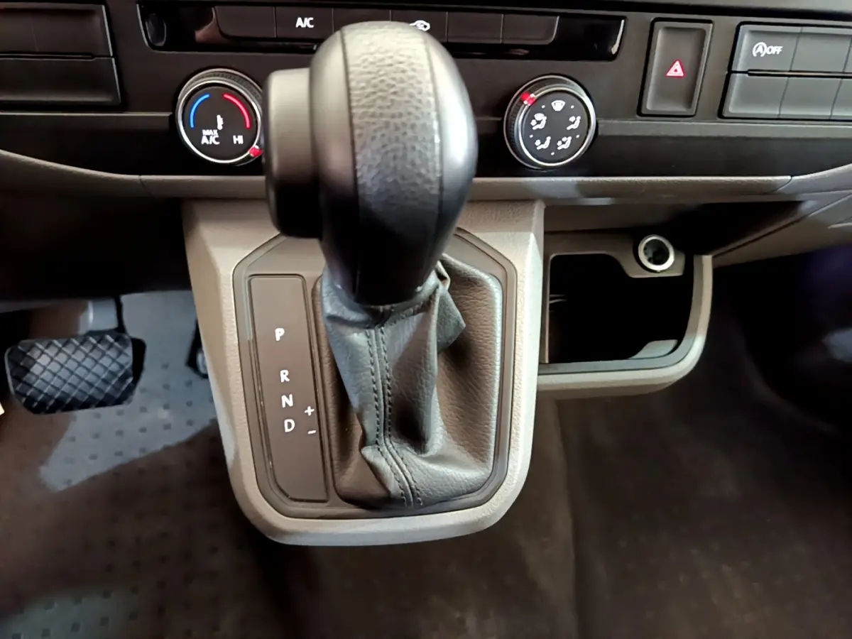 Gros plan sur le levier de vitesses automatique noir et gris du Volkswagen Transporter 2.0 TDi 150 DSG7, tableau de bord beige.