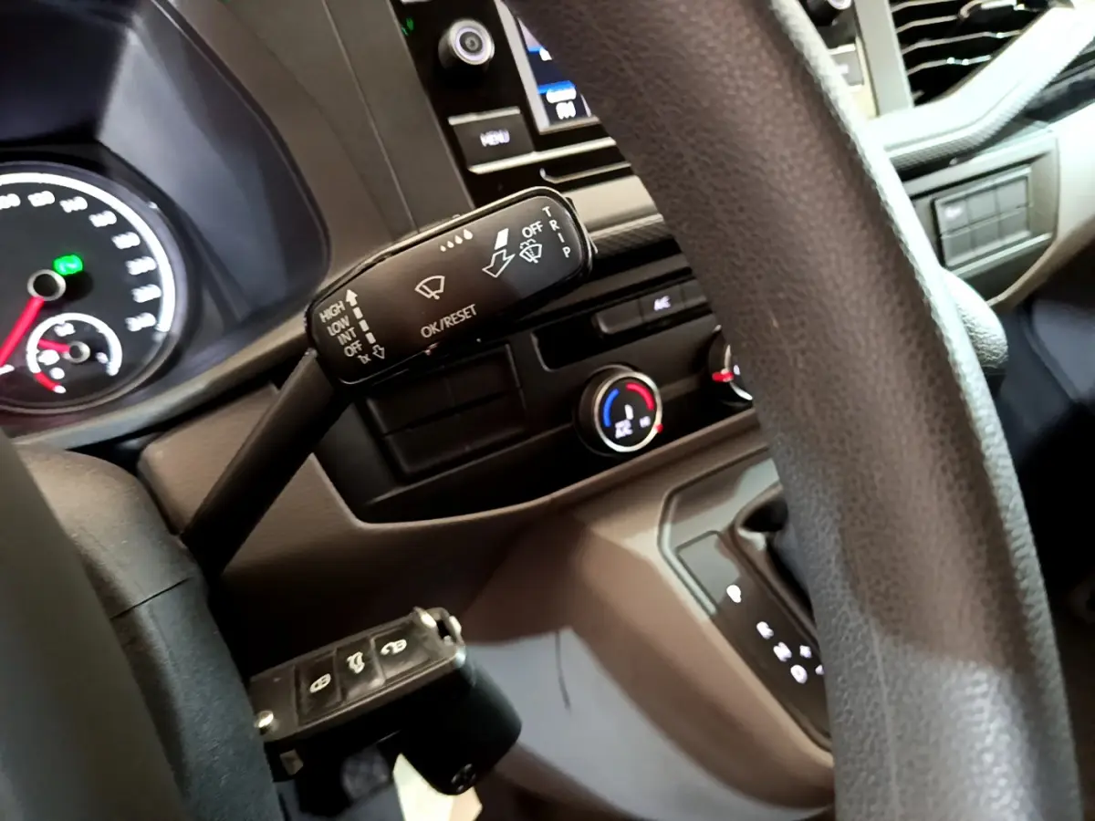 Vue intérieure rapprochée du volant et du tableau de bord du Volkswagen Transporter blanc, avec commandes et écran tactile visibles.