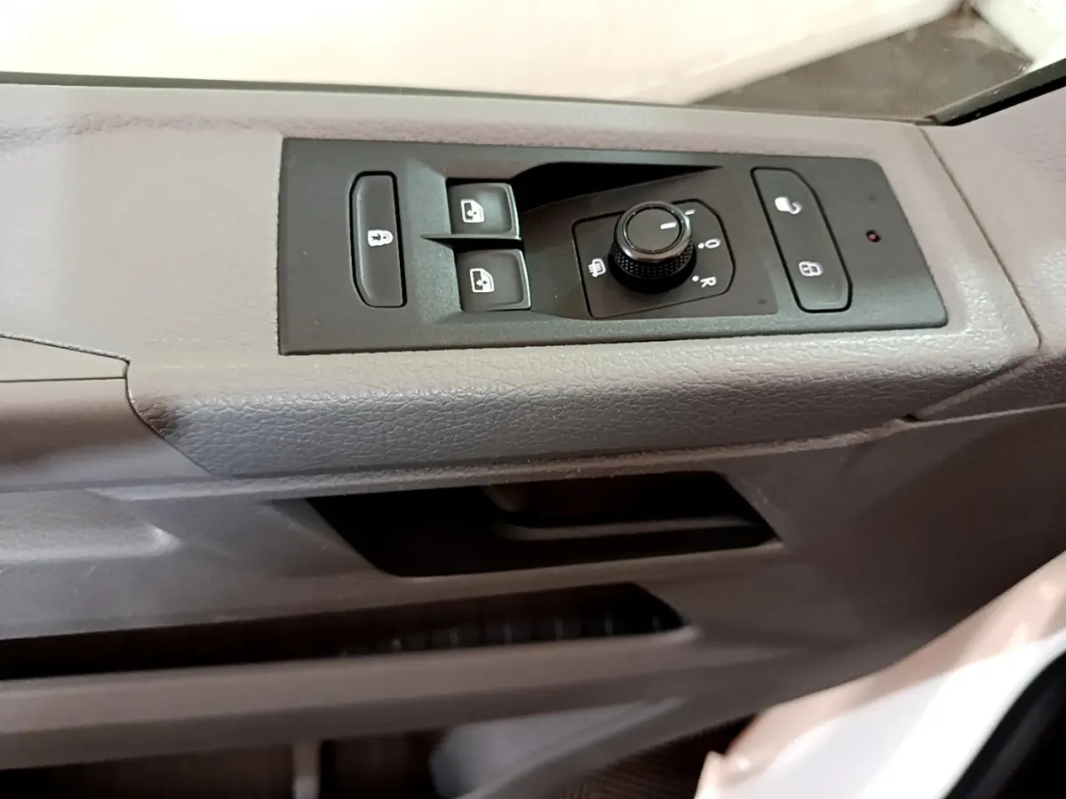 Détail des commandes de lève-vitres et réglage des rétroviseurs sur la porte côté conducteur du Volkswagen Transporter blanc.
