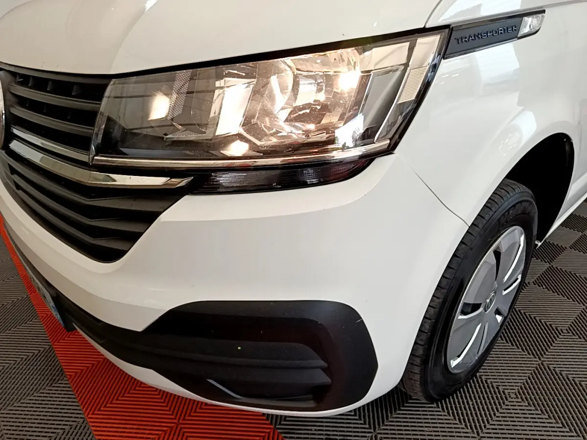 Gros plan sur l'avant droit du Volkswagen Transporter blanc, mettant en valeur le phare allumé et la calandre noire.