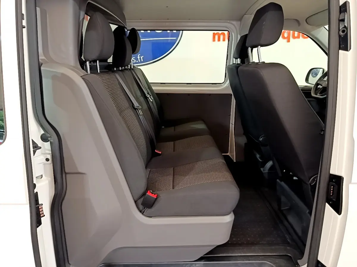 Vue intérieure côté gauche du Volkswagen Transporter blanc 2021, montrant la banquette arrière grise trois places et cloison vitrée.