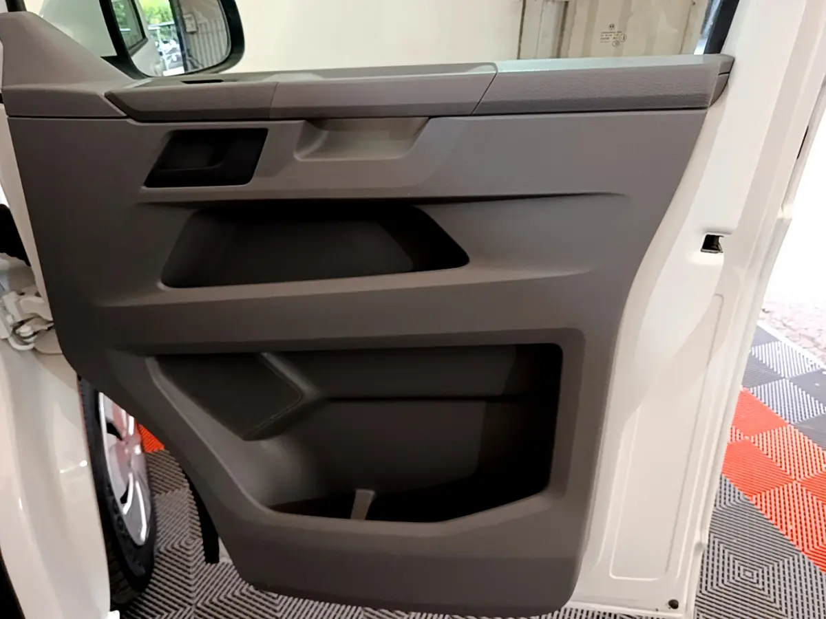 Vue rapprochée de la porte intérieure côté conducteur du Volkswagen Transporter blanc, avec panneau gris et rangement intégré.