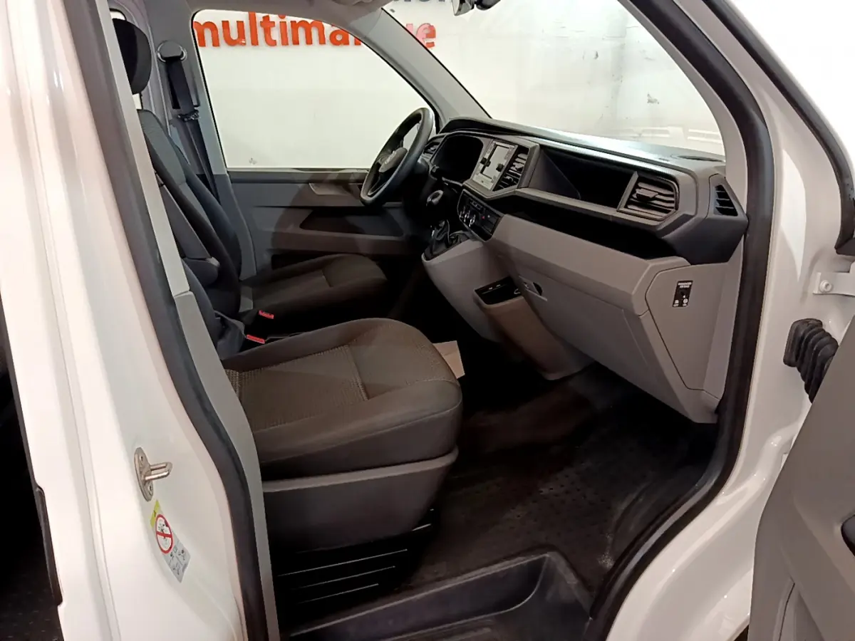 Vue intérieure côté conducteur du Volkswagen Transporter blanc 2021, montrant sièges et tableau de bord moderne.