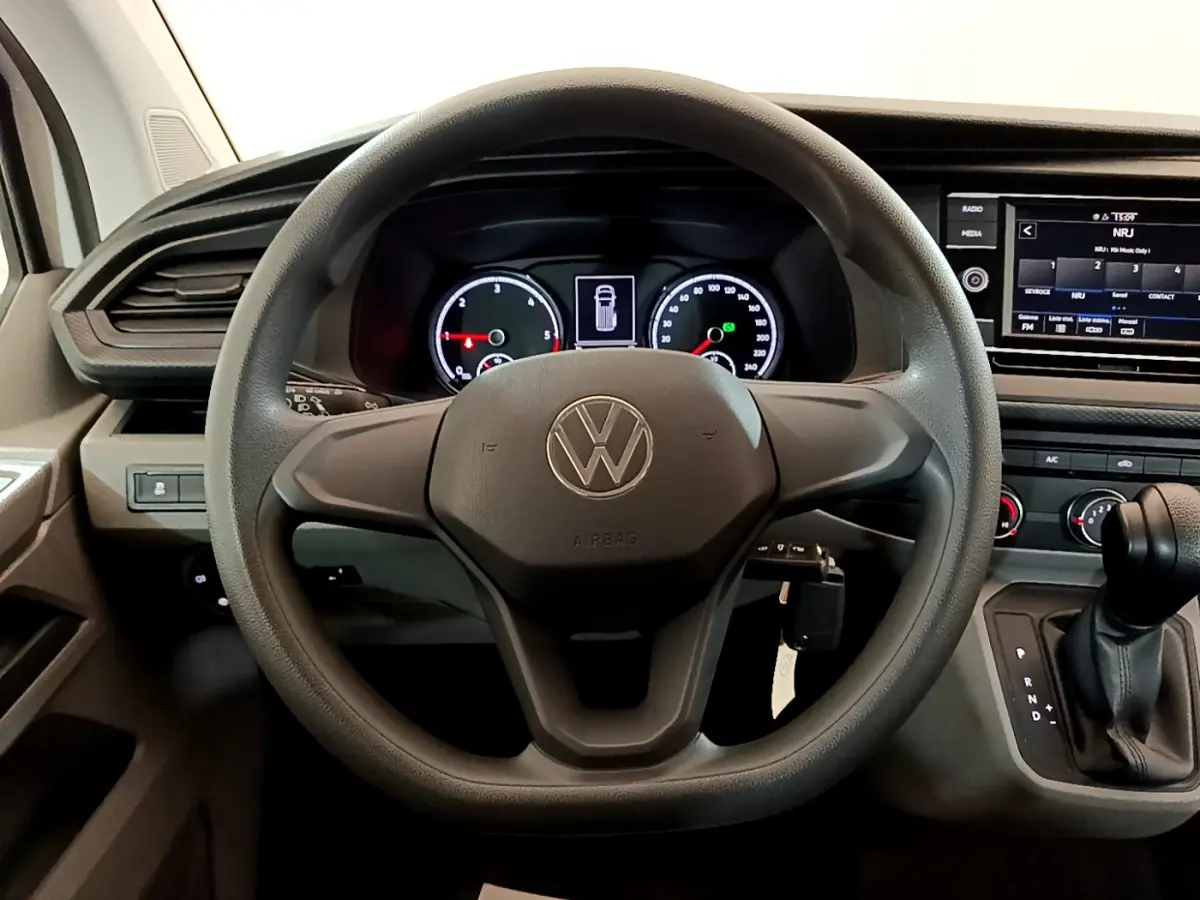 Vue intérieure centrée sur le volant noir du Volkswagen Transporter 2.0 TDi 150 DSG7 avec tableau de bord et écran tactile.