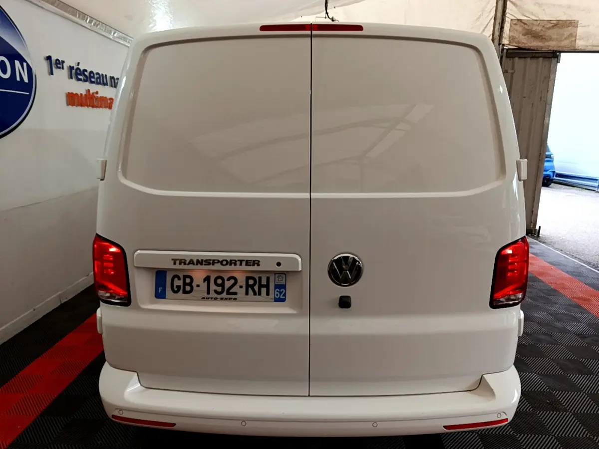 Vue arrière d'un Volkswagen Transporter blanc 2021 avec portes battantes et feux rouges allumés en intérieur.