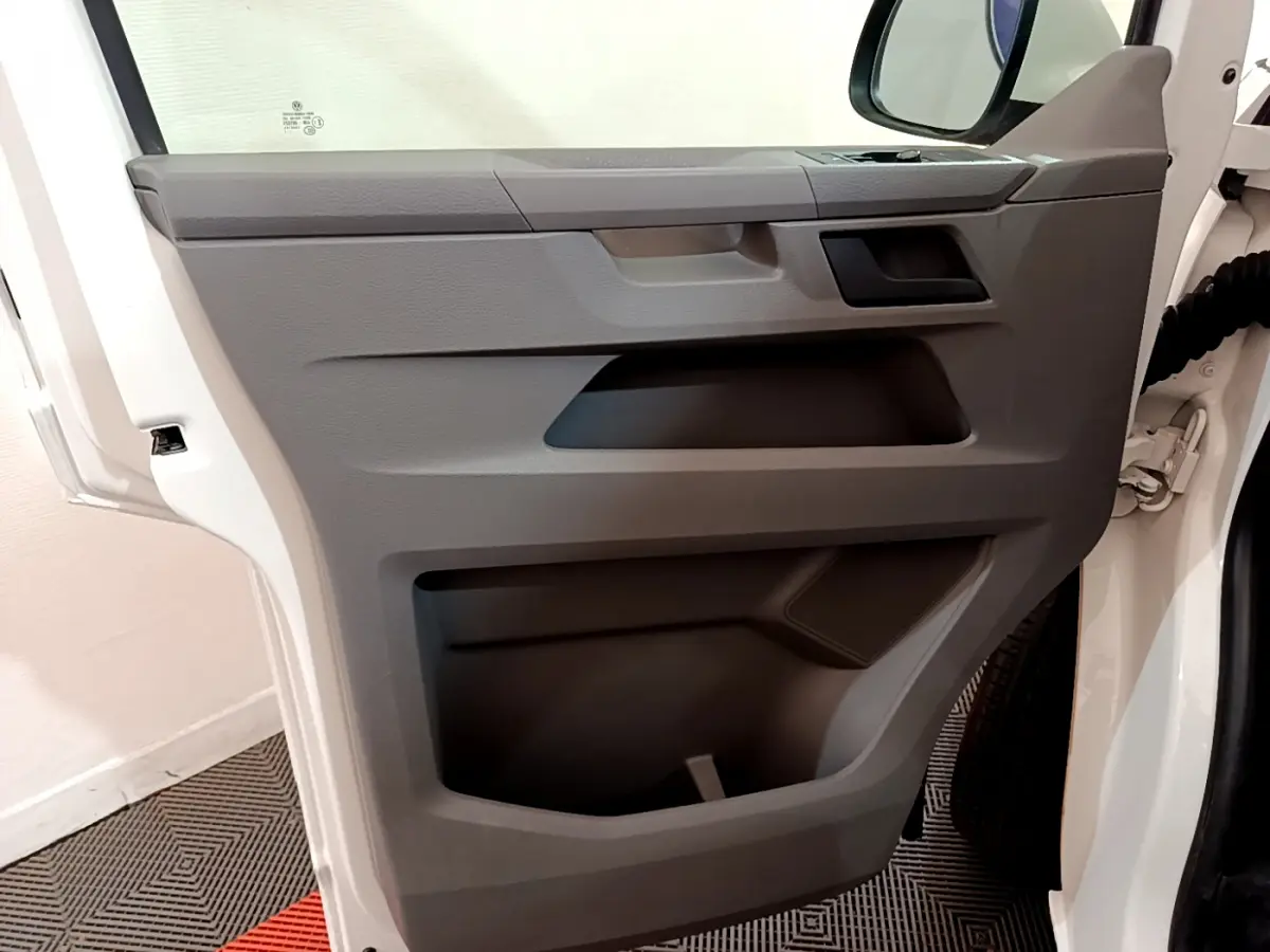 Vue rapprochée de la porte avant gauche blanche du Volkswagen Transporter 2.0 TDi 150 DSG7 avec panneaux gris et rangements intégrés.