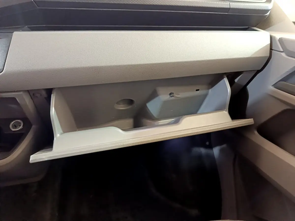 Vue intérieure du vide-poche ouvert côté passager du Volkswagen Transporter blanc, montrant son rangement spacieux.