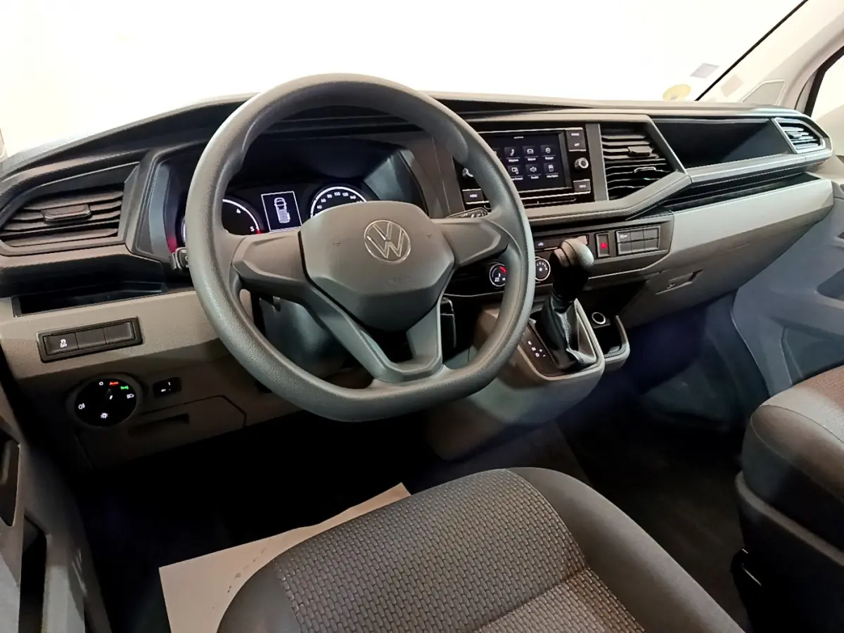 Vue intérieure avant du tableau de bord et volant noir du Volkswagen Transporter blanc, avec écran tactile central et levier de vitesses.