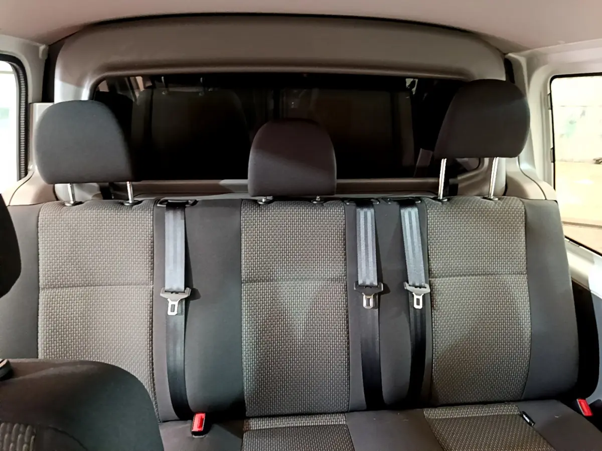 Vue intérieure arrière montrant la banquette trois places grise du Volkswagen Transporter blanc avec ceintures de sécurité.