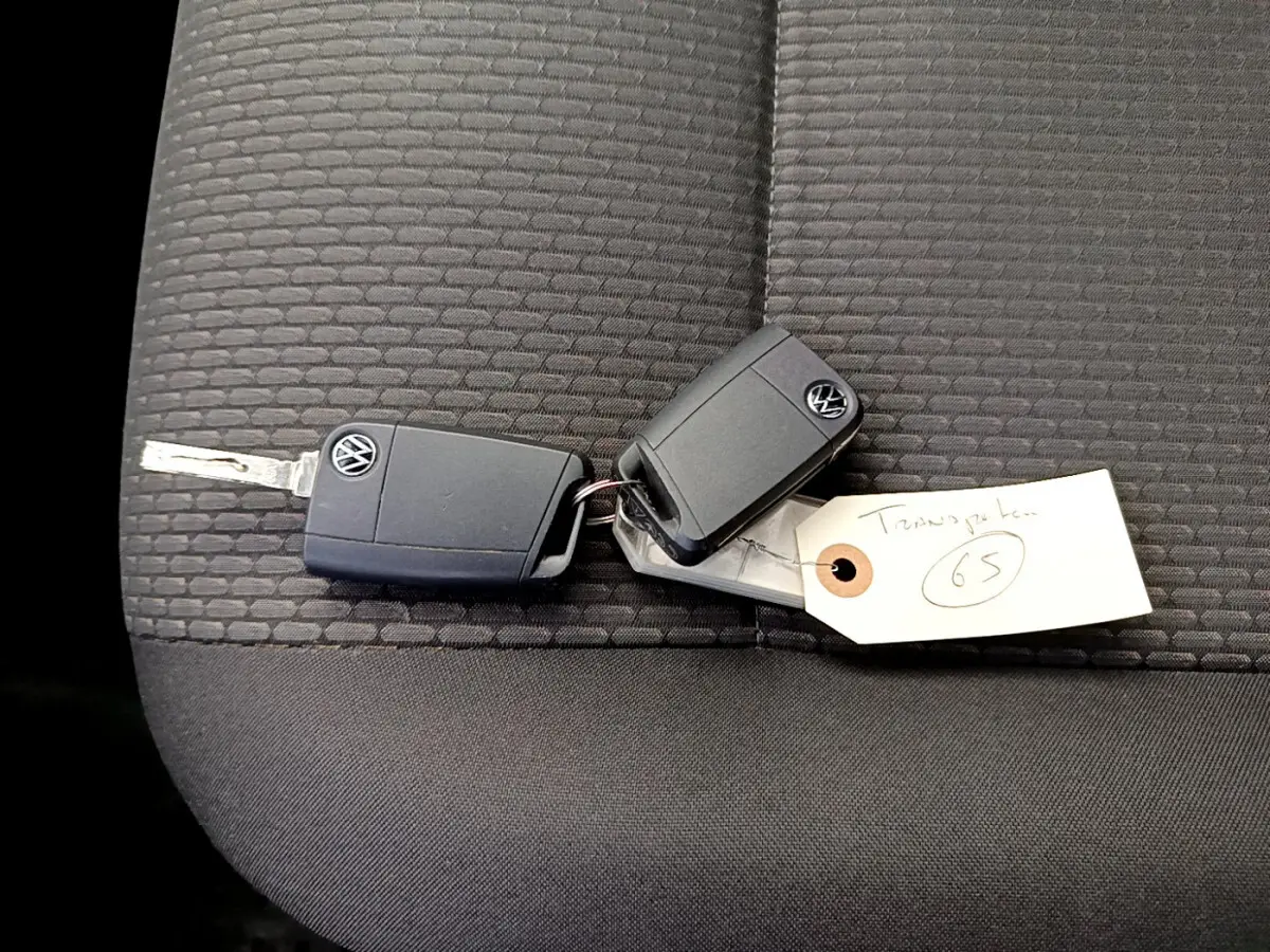 Clé Volkswagen posée sur un siège tissu gris foncé à motifs, avec une étiquette manuscrite attachée.