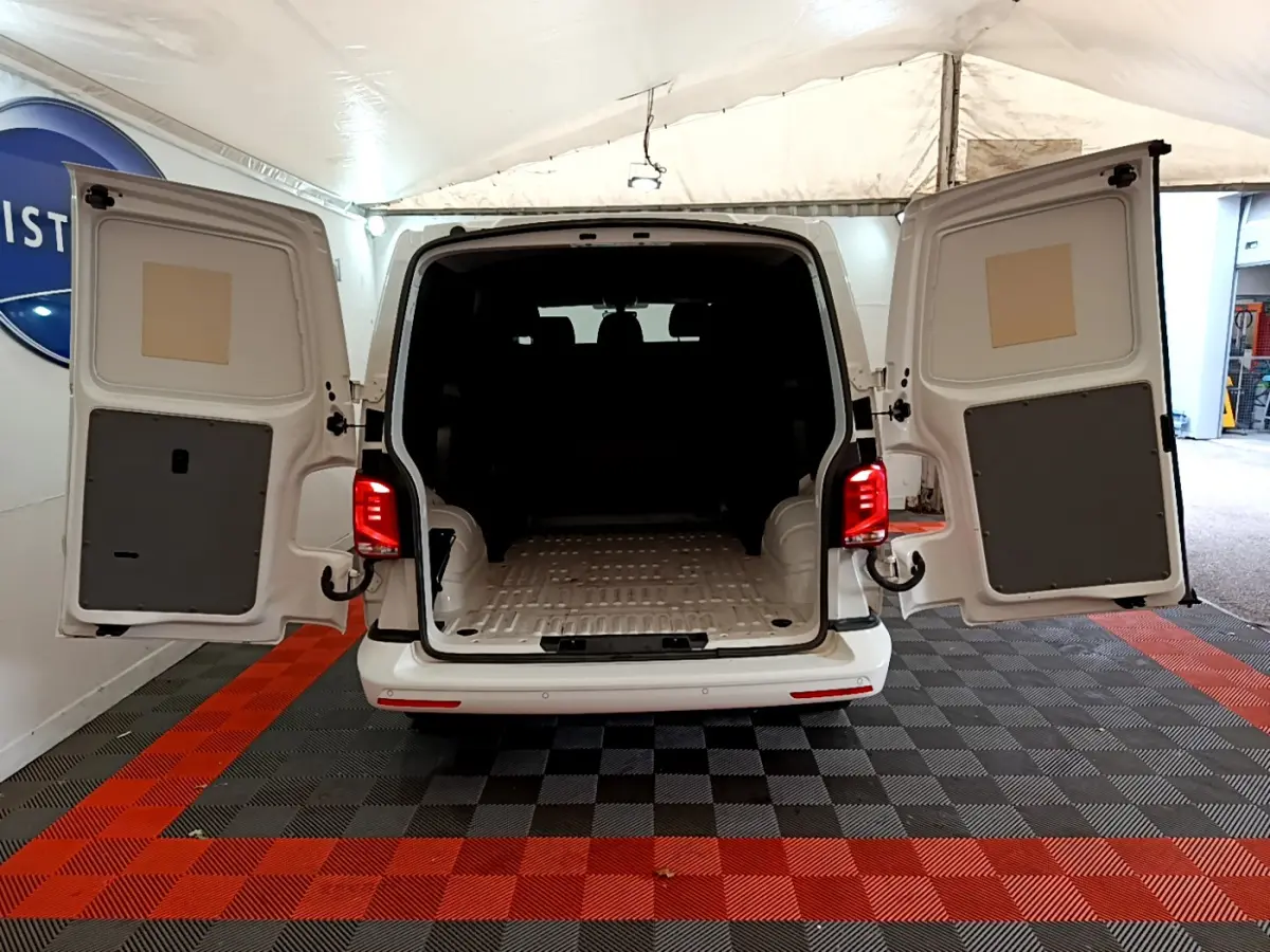 Vue arrière d’un Volkswagen Transporter blanc 2021 avec portes arrière ouvertes et espace de chargement visible.