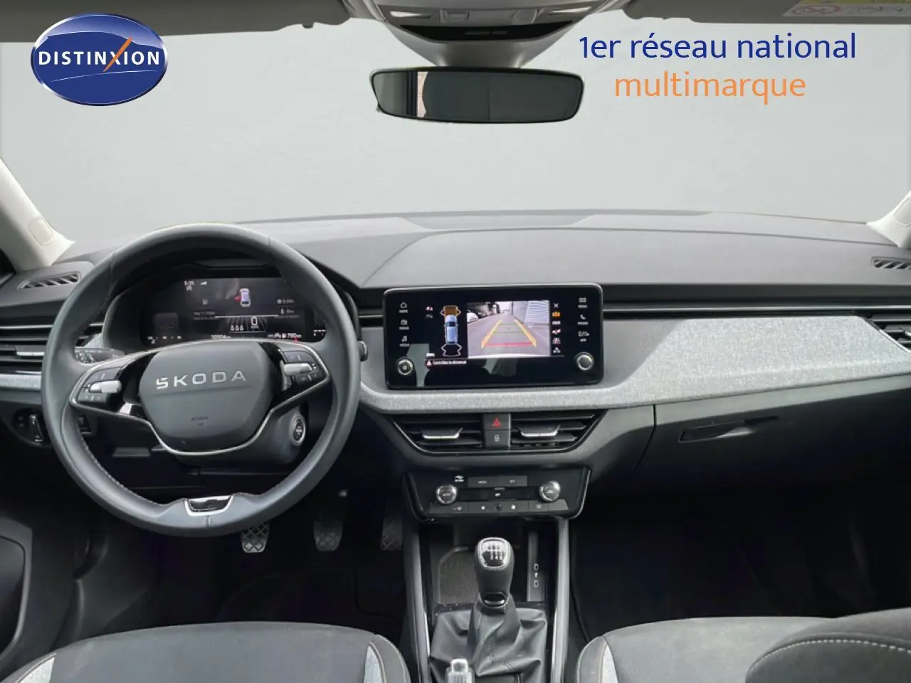 Vue intérieure frontale du tableau de bord gris noir de la Skoda Scala 2025 avec volant cuir et écran tactile central.