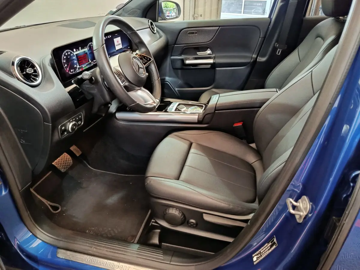 Intérieur côté conducteur du Mercedes GLA 250 e bleu 2024, volant cuir, tableau de bord digital et sièges noirs cuir.