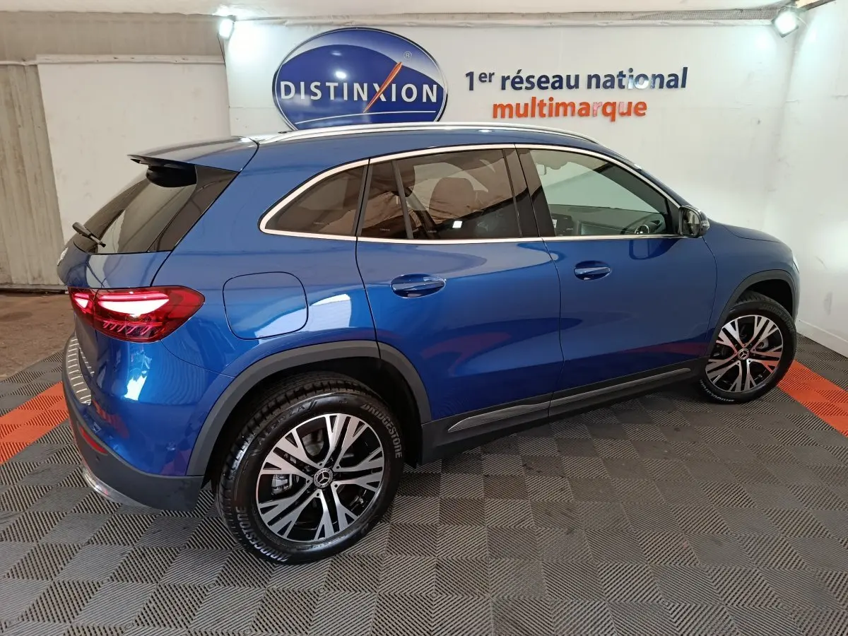 Vue 3/4 arrière droite d'un Mercedes GLA 250 e Business Line bleu avec jantes alliage et toit noir dans un showroom.