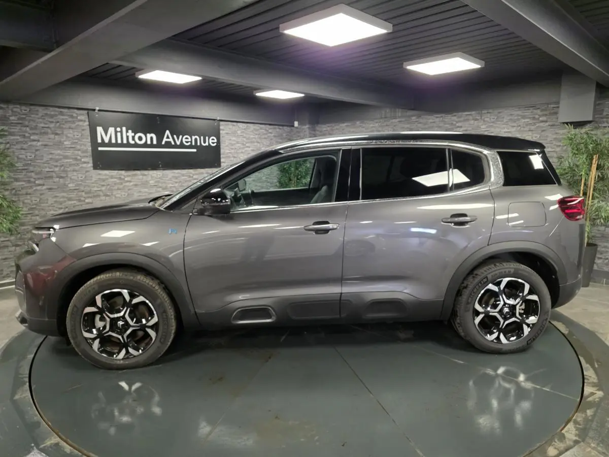 Profil côté gauche du Citroën C5 Aircross Hybrid gris avec toit noir et jantes alliage bi-ton dans un showroom.