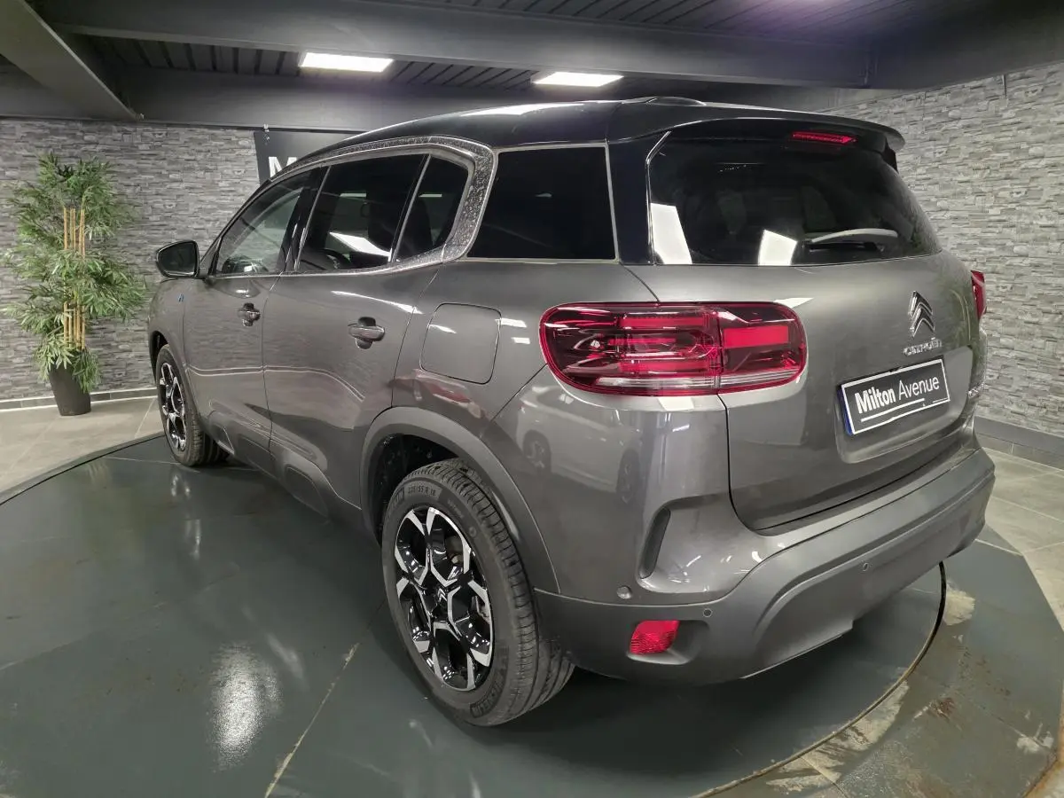 Vue 3/4 arrière droite d'un Citroën C5 Aircross Hybrid gris métallisé avec toit noir et jantes bi-ton 18 pouces.