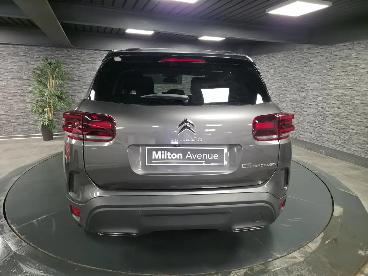 Vue arrière d'un Citroën C5 Aircross gris métallisé avec toit noir et feux arrière LED en intérieur showroom.