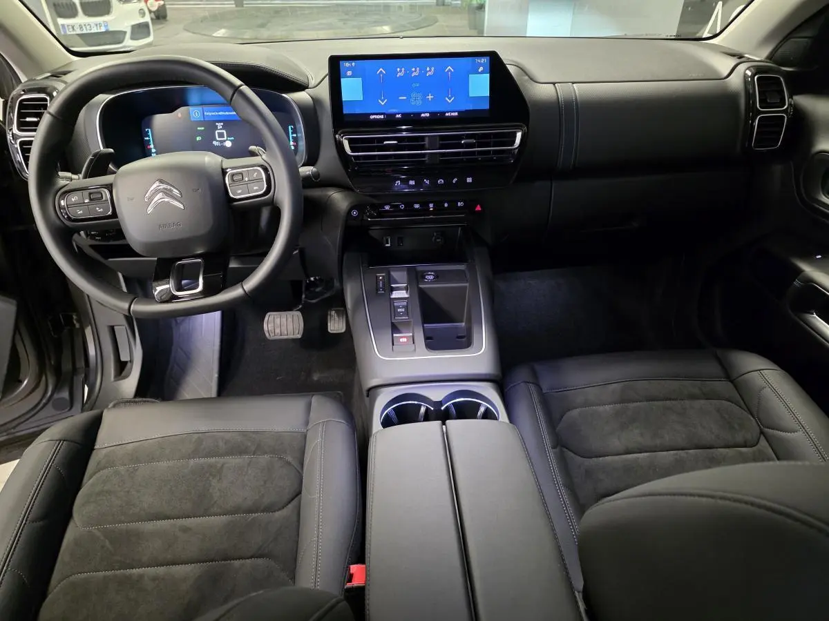 Intérieur noir du Citroën C5 Aircross Hybrid 2024, vue avant sur volant, tableau de bord et console centrale tactile.