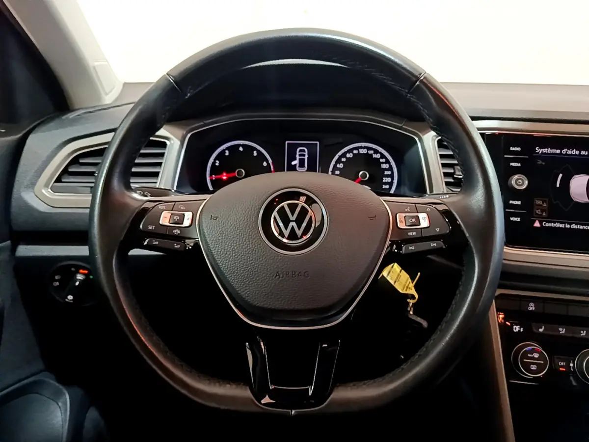 Vue intérieure centrée sur le volant cuir noir du Volkswagen T-Roc 1.0 TSI 110 Lounge avec tableau de bord digital.