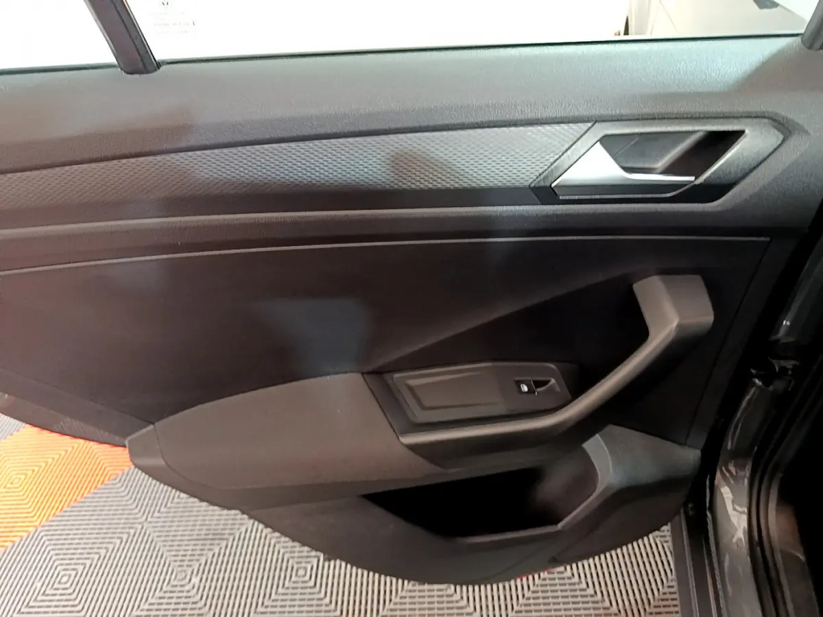 Vue intérieure côté gauche de la porte avant gris foncé du Volkswagen T-Roc 1.0 TSI 110 Lounge avec poignée angulaire et bouton de vitre électrique.