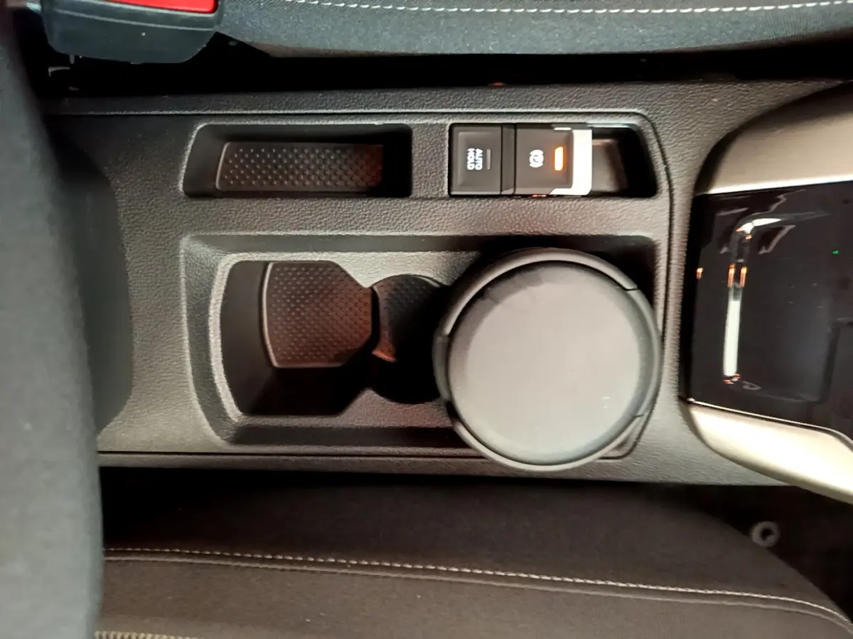 Gros plan sur la console centrale noire du Volkswagen T-Roc 1.0 TSI 110 Lounge, avec frein à main électrique et porte-gobelet.
