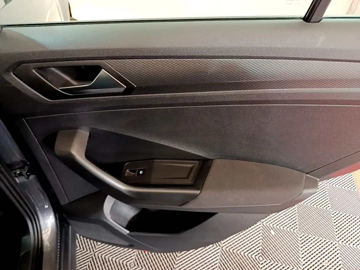 Gros plan sur la porte intérieure côté conducteur du Volkswagen T-Roc gris foncé, avec poignée et commande de vitre.