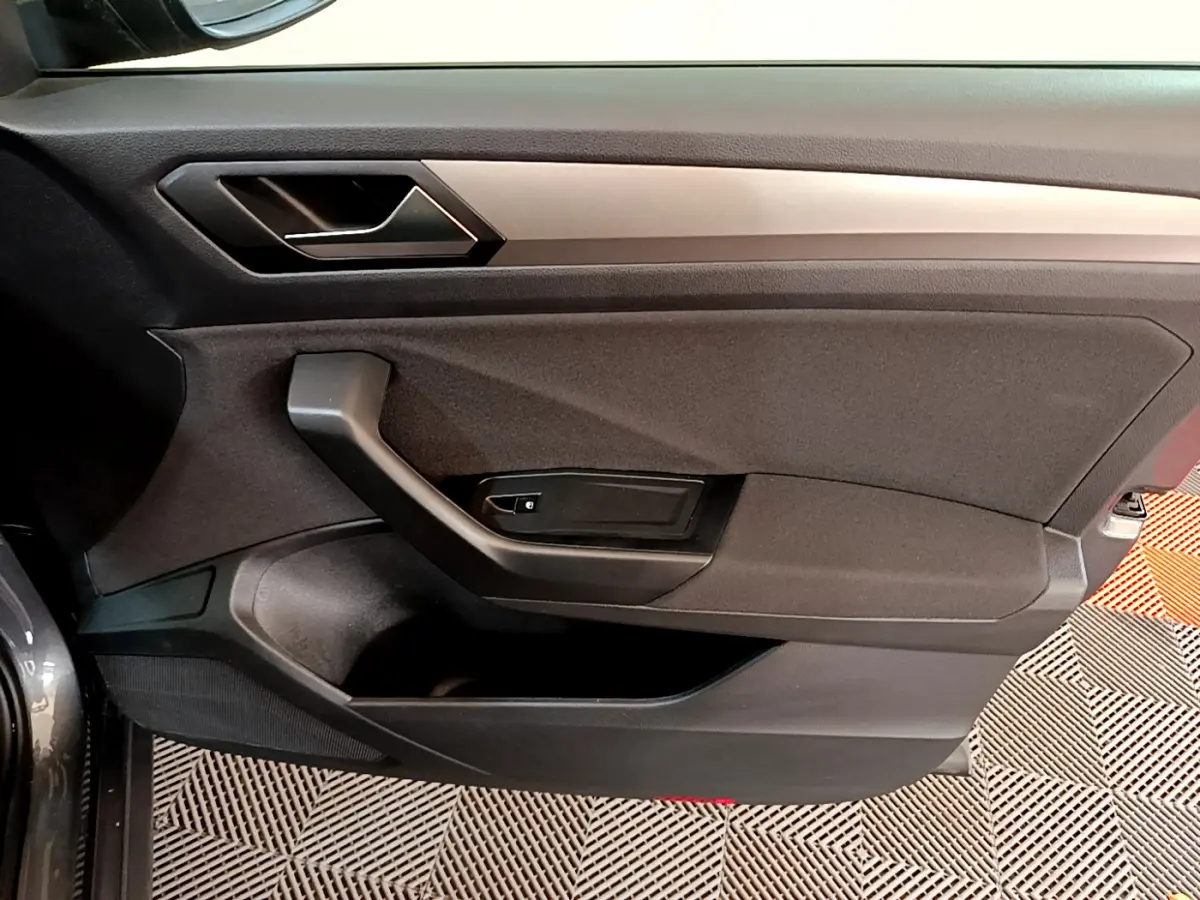 Vue intérieure côté gauche de la porte avant gris foncé du Volkswagen T-Roc 1.0 TSI 110 Lounge avec poignée et panneau noir.