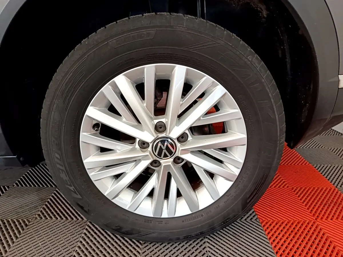 Gros plan sur la roue avant droite d’un Volkswagen T-Roc gris foncé, jante alliage argentée à multiples branches.