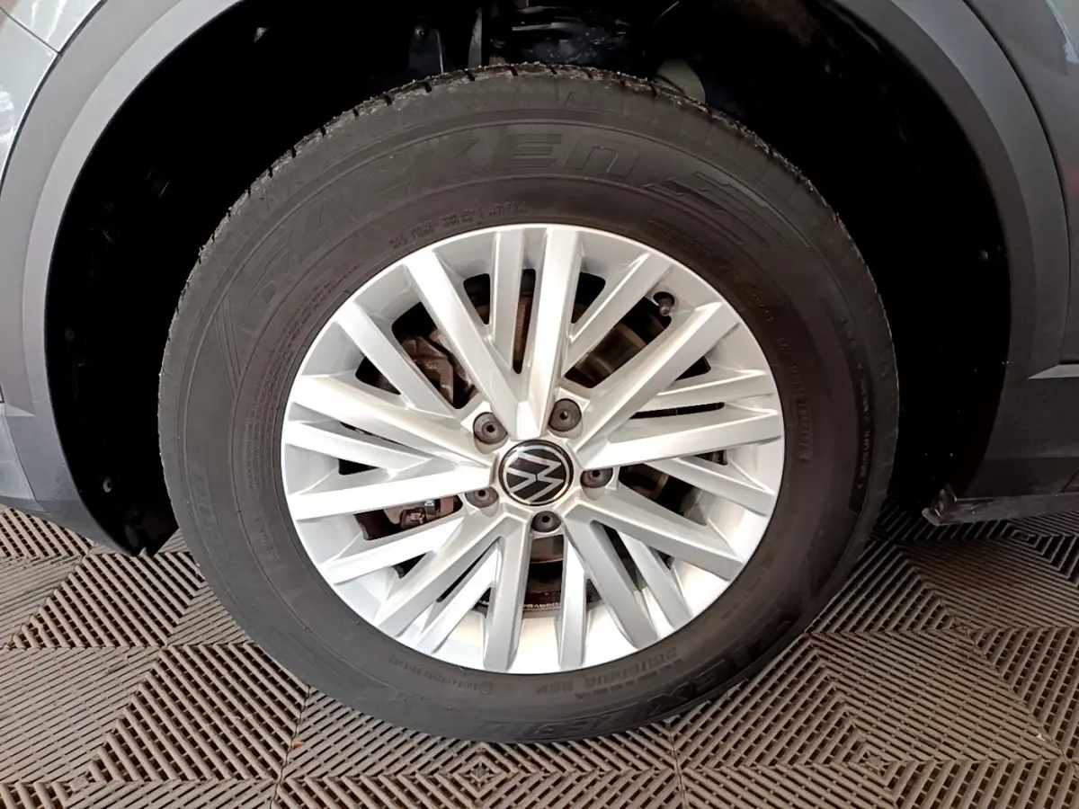 Gros plan sur la roue avant droite d’un Volkswagen T-Roc gris foncé avec jante alliage argentée à multiples branches.