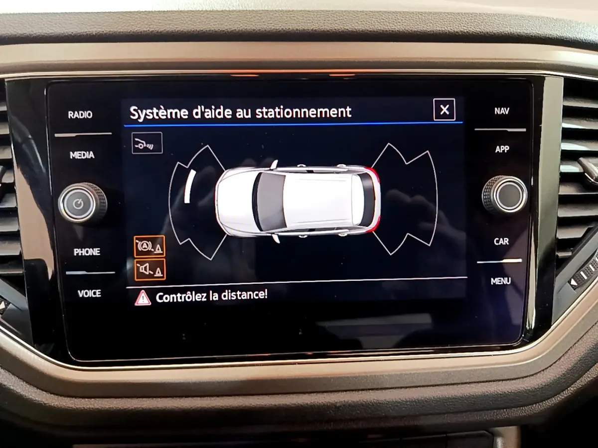 Écran tactile du système d'aide au stationnement affichant une vue aérienne du Volkswagen T-Roc gris foncé.