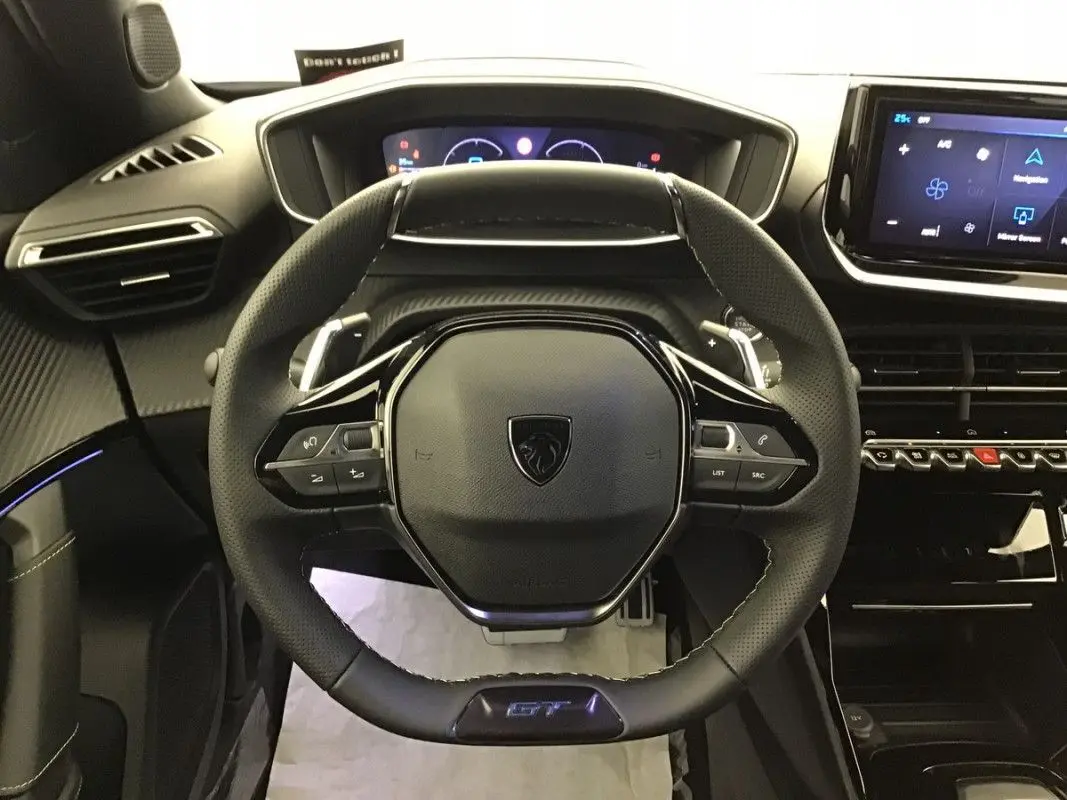 Vue frontale du volant cuir noir avec logo Peugeot et badge GT du tableau de bord du Peugeot 2008 Hybrid 2025.