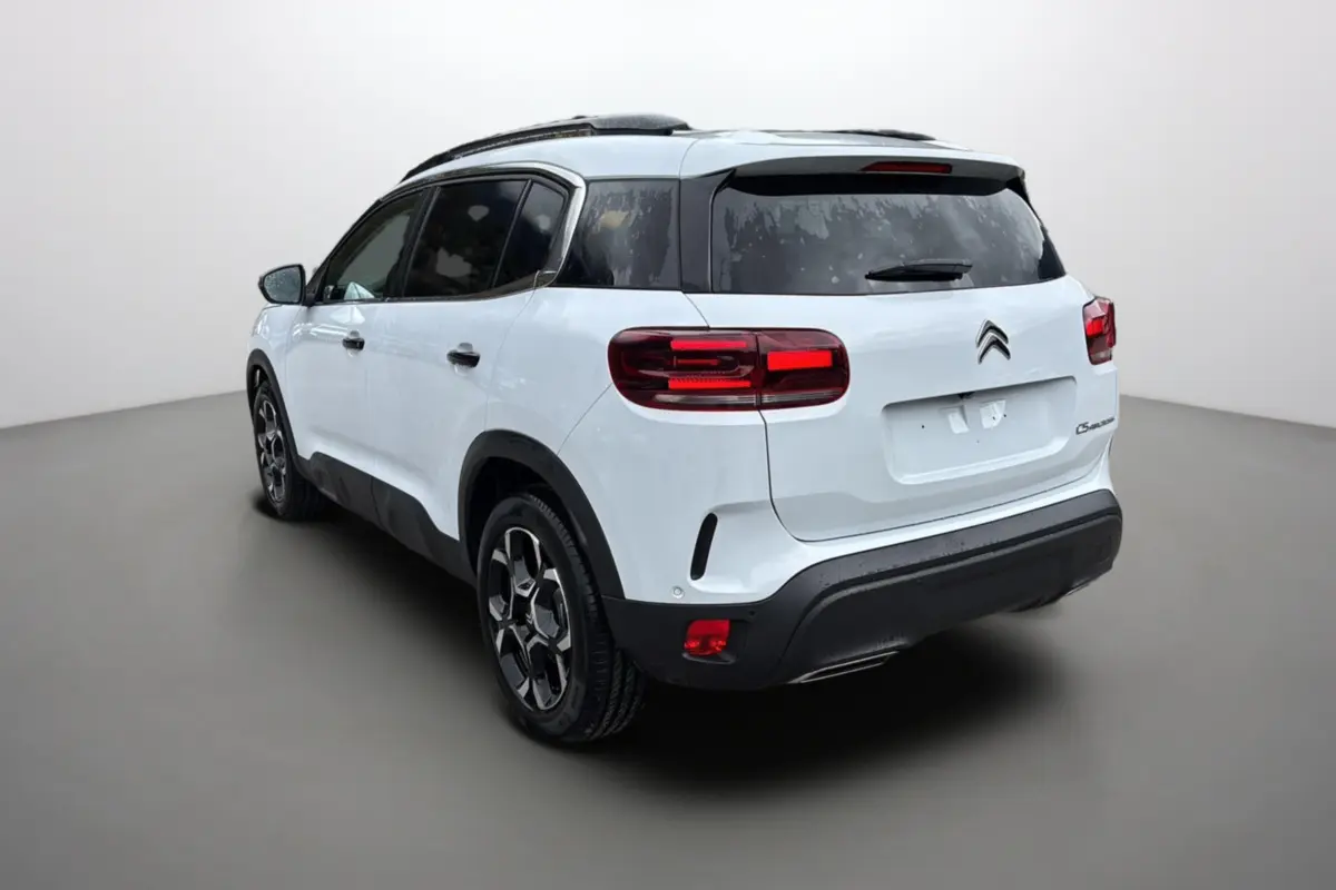 Vue 3/4 arrière droite d’un Citroën C5 Aircross Hybrid blanc okénite avec barres de toit et vitres surteintées.