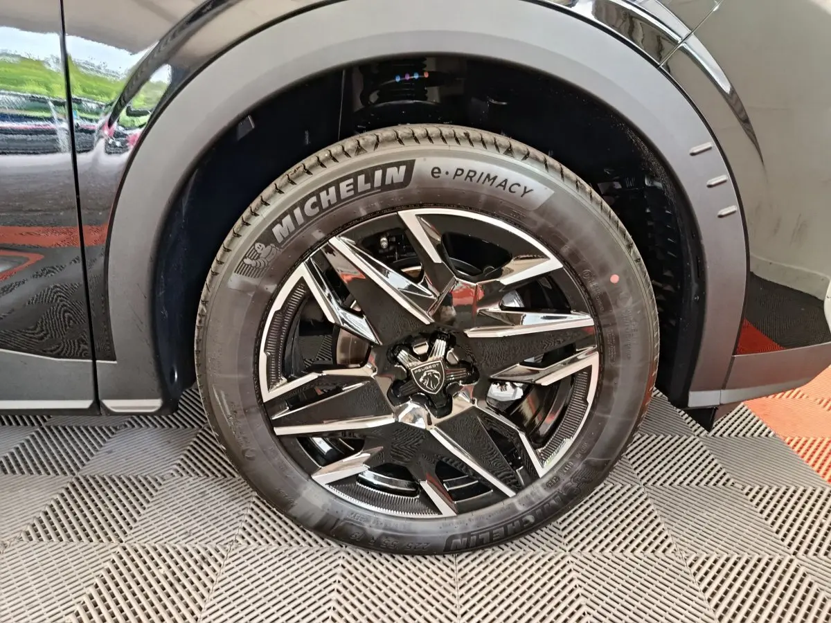 Gros plan sur la roue avant gauche noire du Peugeot 3008 1.2 HYBRID 145 GT avec jante en alliage chromée et pneu Michelin.