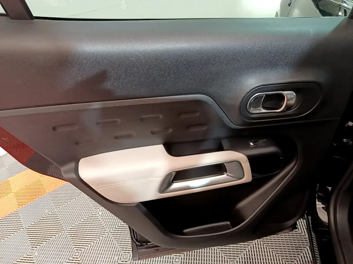 Vue rapprochée de la porte intérieure côté gauche du Citroën C5 Aircross Hybrid 225 noir, avec accoudoir beige et poignée chromée.